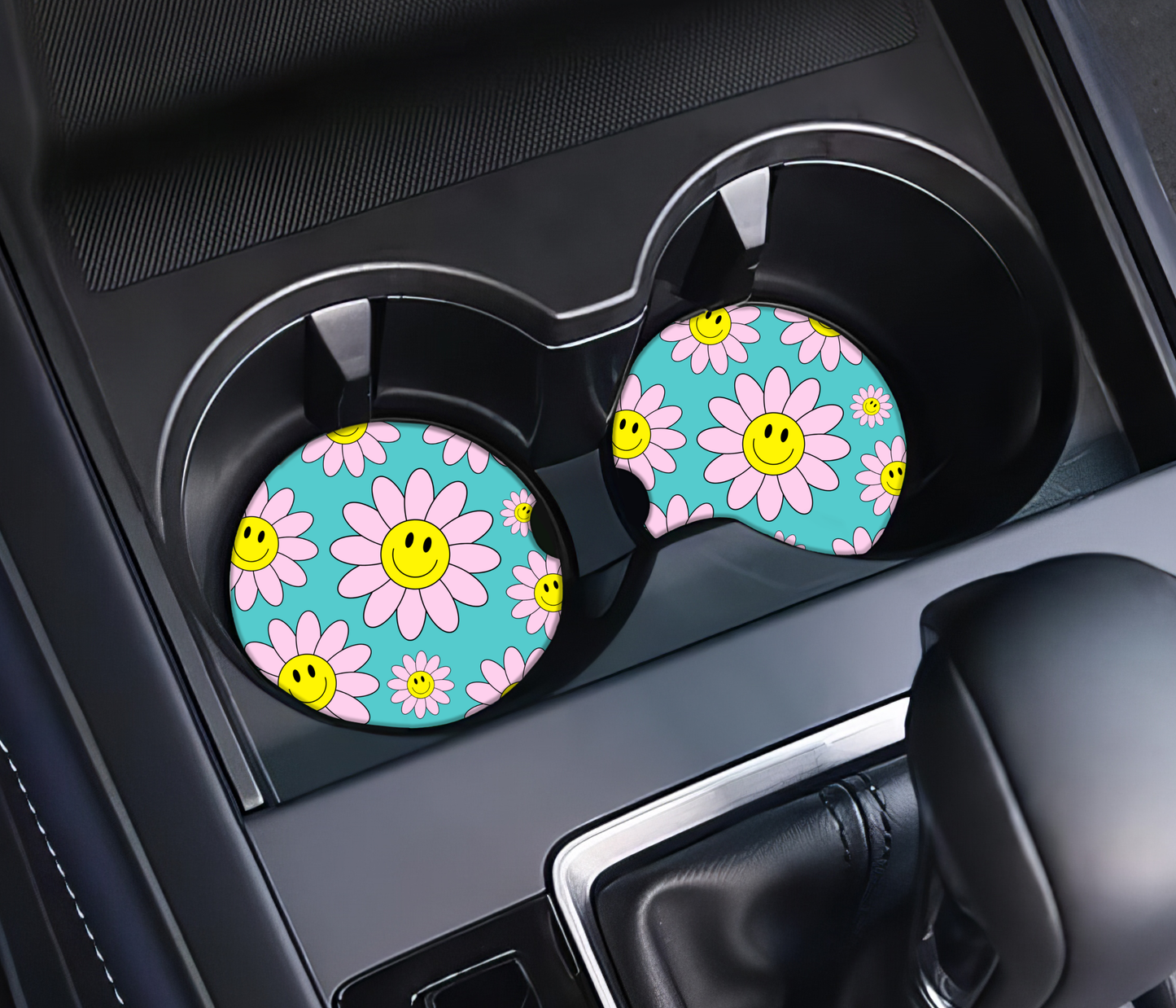 Two car cup holders with floral and smiley face design coasters in a vehicle.