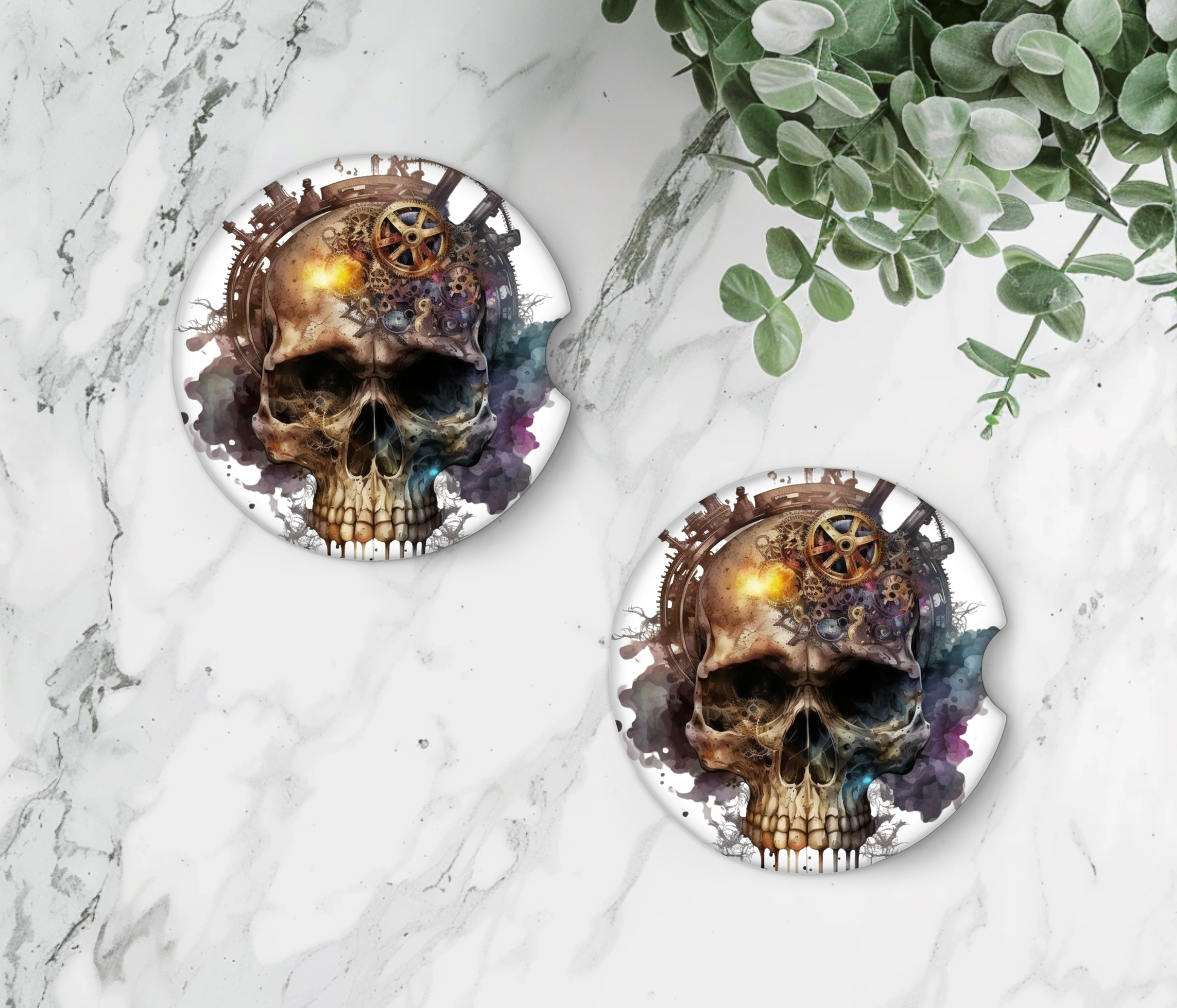 Two round coasters with skull designs on a marble surface with greenery.
