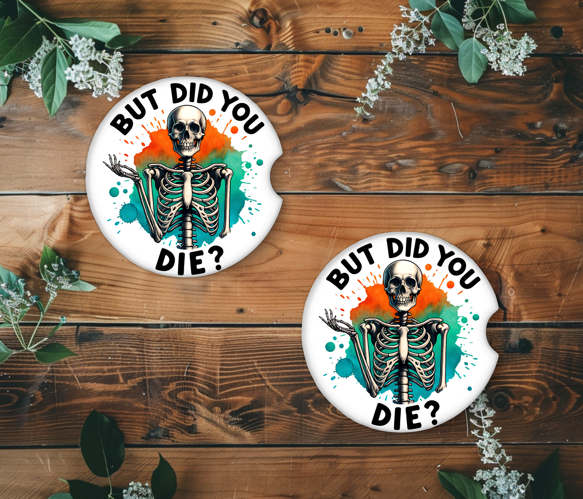 Two circular coasters with a skeleton design and 'But Did You Die?' text on a wooden surface with greenery.