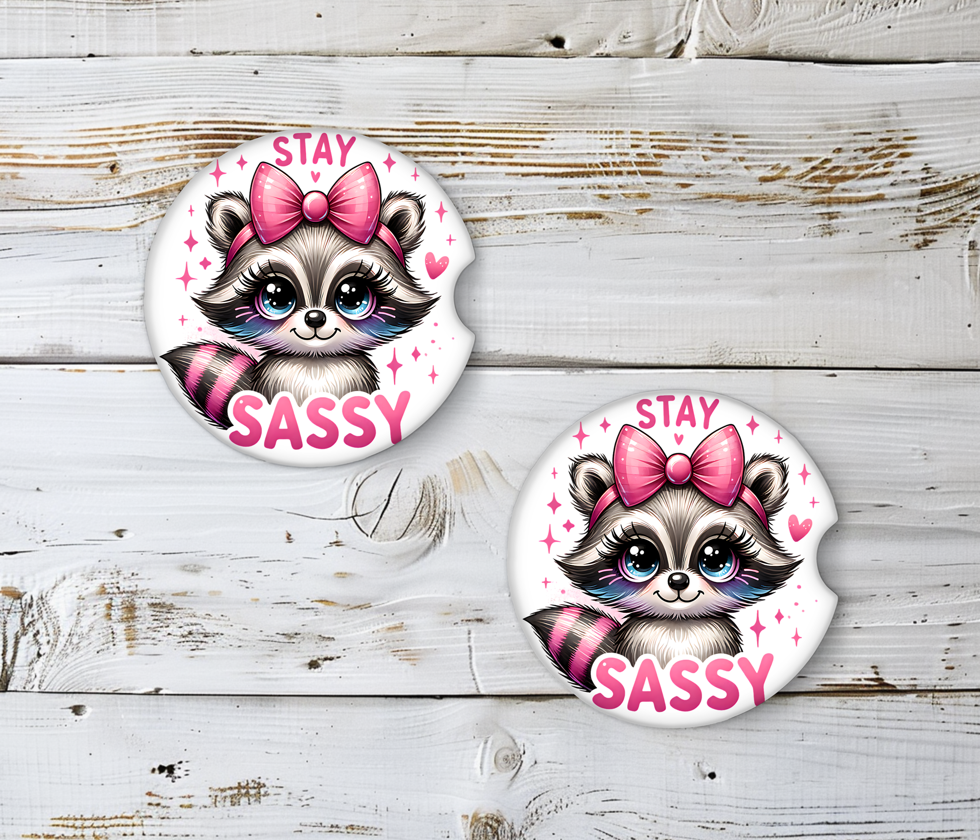 Two round stickers with a raccoon design and 'Stay Sassy' text on a wooden surface.