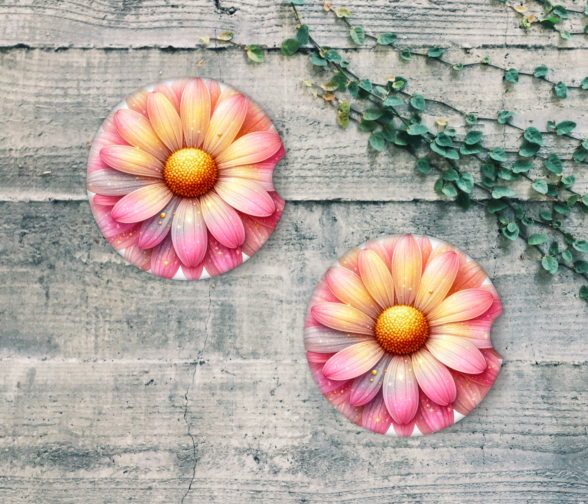 Two pink flower coasters on a textured wooden surface with green leaves.