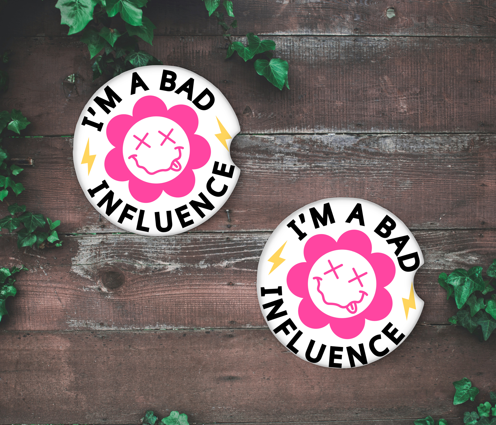 Two 'I'm a Bad Influence' stickers on a wooden surface with green leaves around.