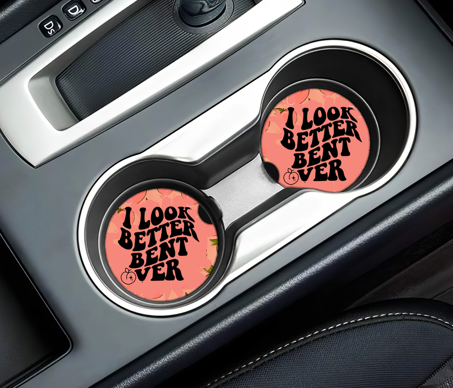 Two pink car coasters with text in a car's cup holder.