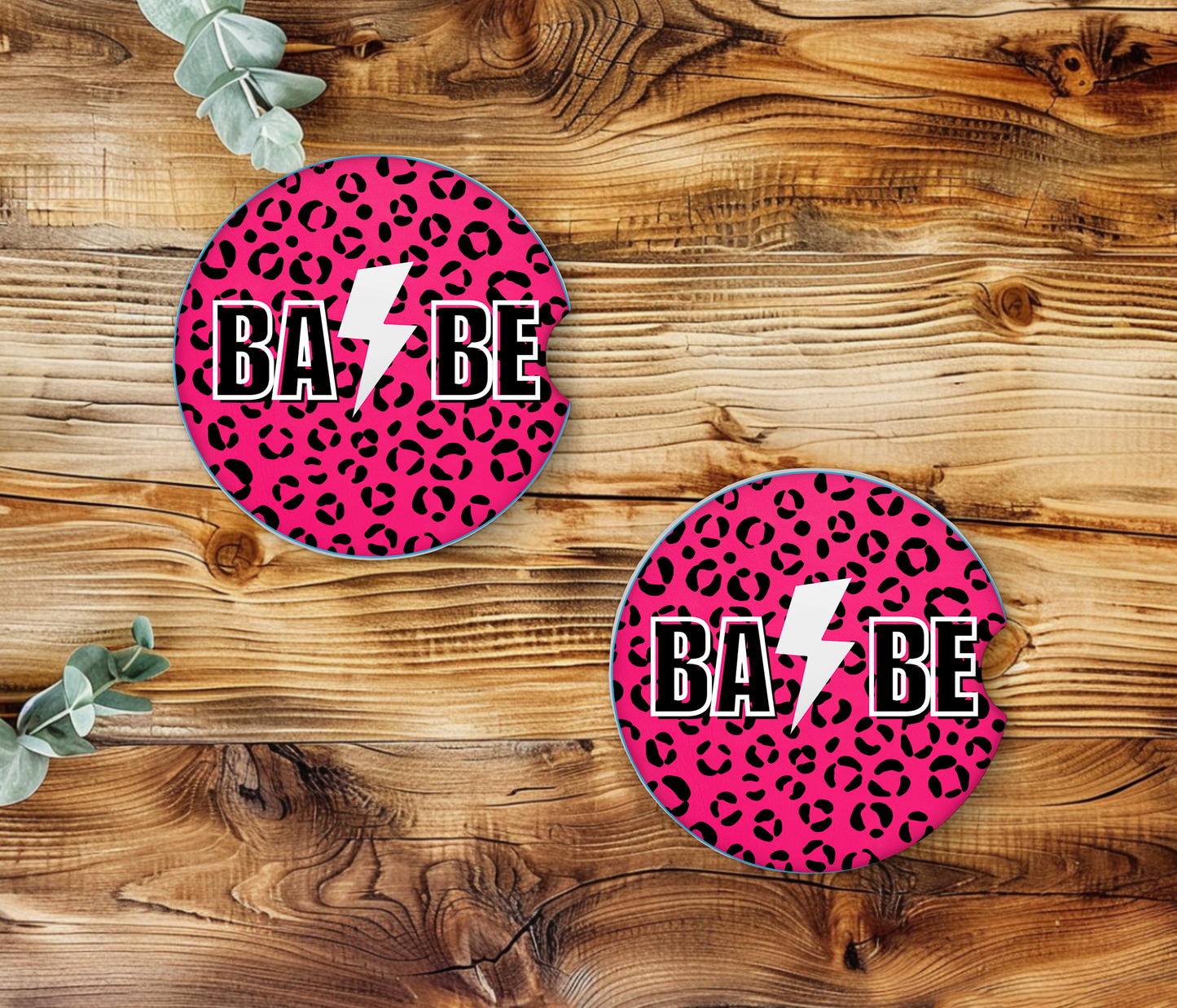 Two pink leopard print coasters with 'BA BE' text on a wooden surface.